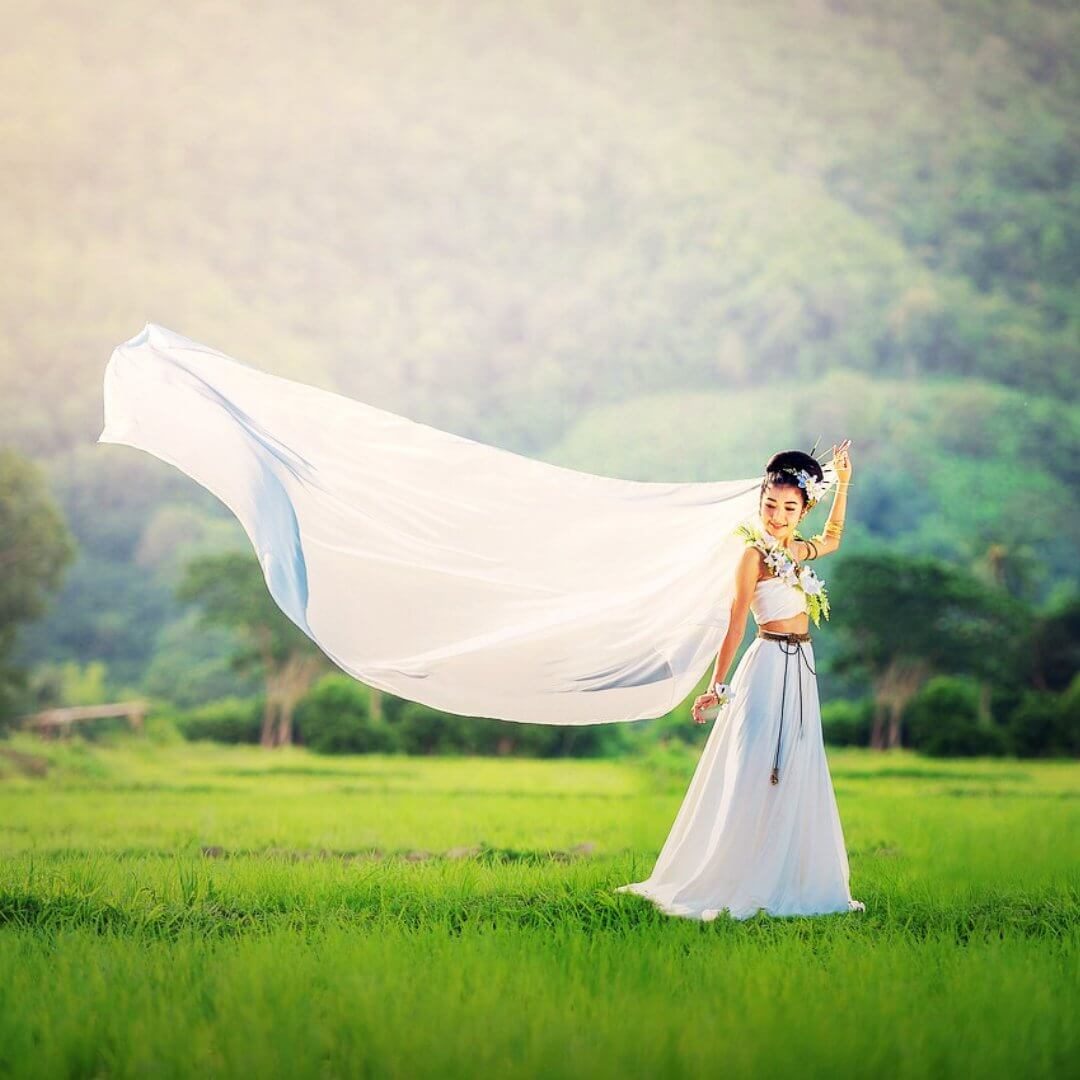 Eine Frau in einem traditionellen weißen Hochzeitskleid mit langem Schleier in Pattaya, Thailand, umgeben von grüner Natur.