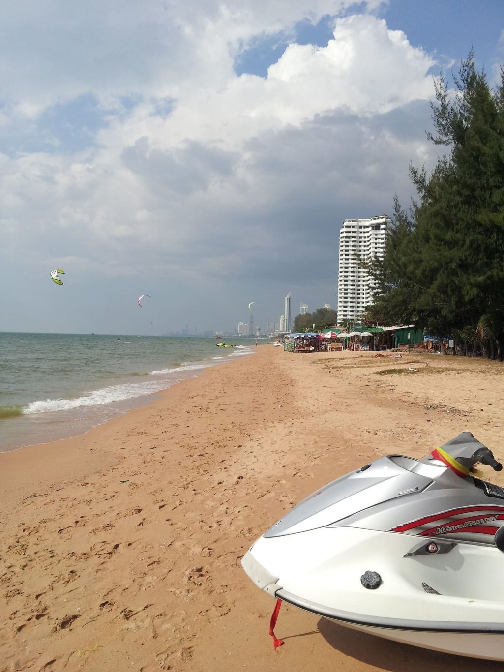 ag am Pattaya Beach in Thailand, mit Jet-Ski im Vordergrund und Kitesurfern am Himmel