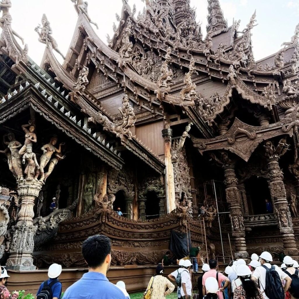 Geführte Tour am Sanctuary of Truth Pattaya, Thailand Besuchergruppe mit Helmen vor der kunstvoll geschnitzten Holzfassade des Sanctuary of Truth in Pattaya während einer geführten Tempeltour.